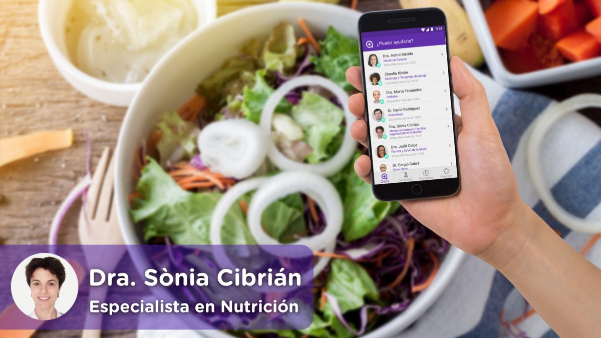 móvil con la aplicación de chat médico de mediquo. Cocina con plato lleno de alimentos saludables, ensalada, fruta, cebolla, patatas, etc. Nutricionista Dra. Sònia Cibrian