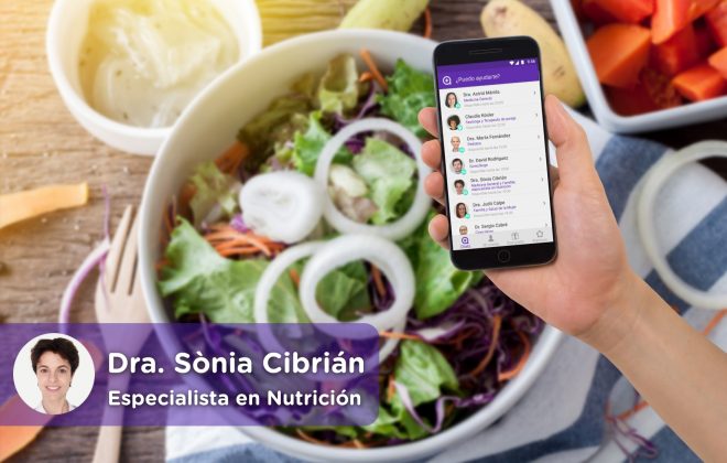 móvil con la aplicación de chat médico de mediquo. Cocina con plato lleno de alimentos saludables, ensalada, fruta, cebolla, patatas, etc. Nutricionista Dra. Sònia Cibrian